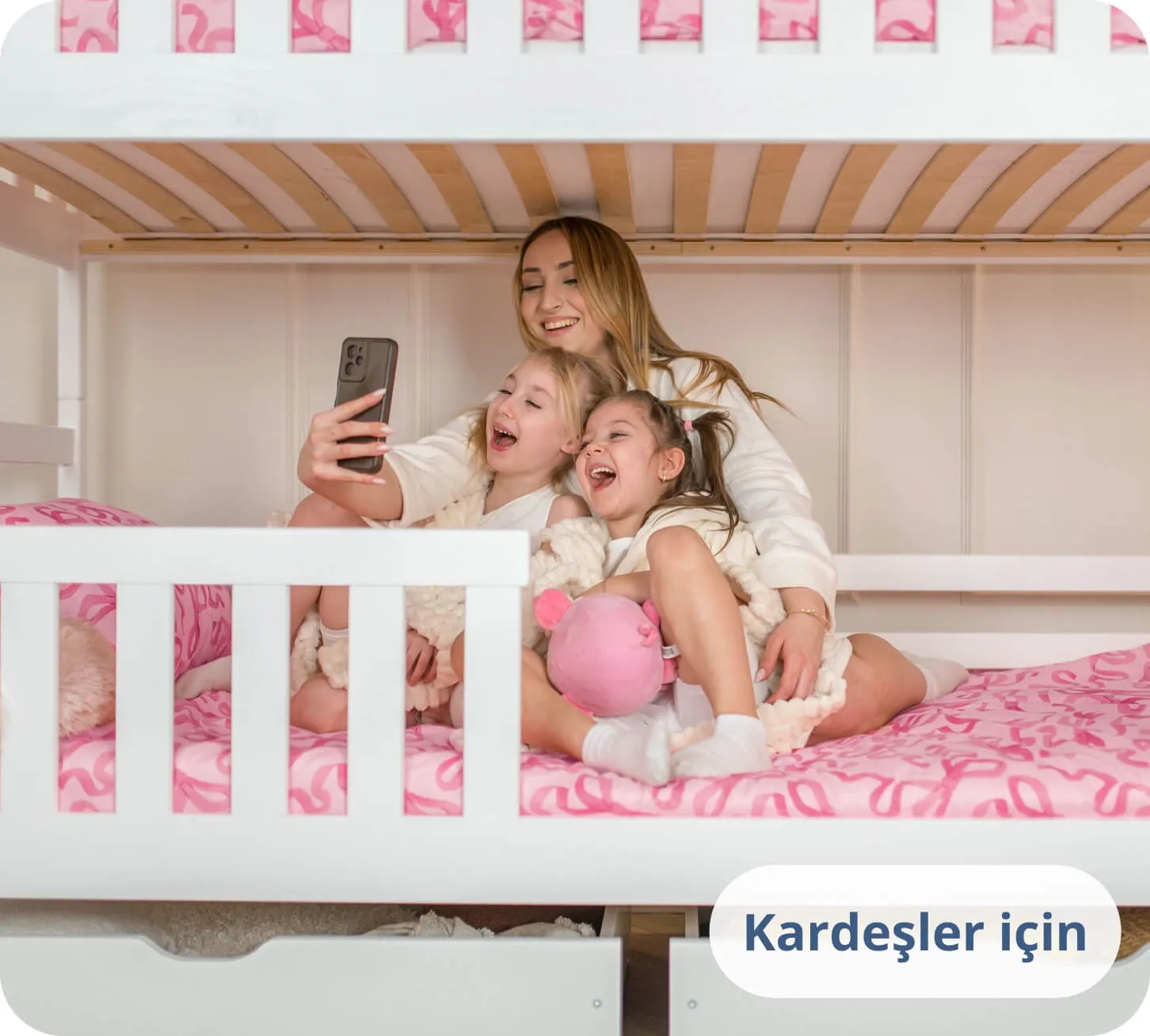Beyaz bir ranzada telefona bakarak gülen iki kız çocuğu ve bir kadın.